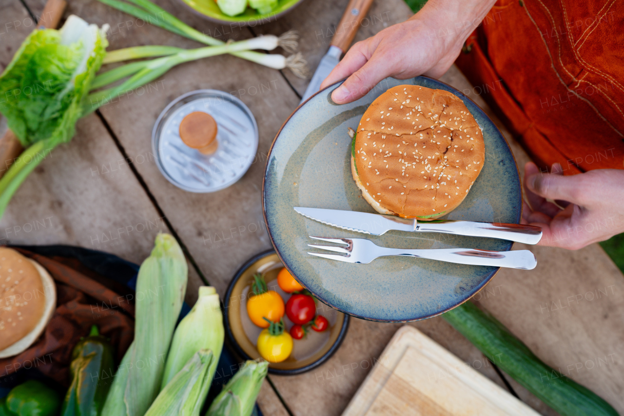 Top view of man holding plate with homemade grilled hamburger and cutlery.