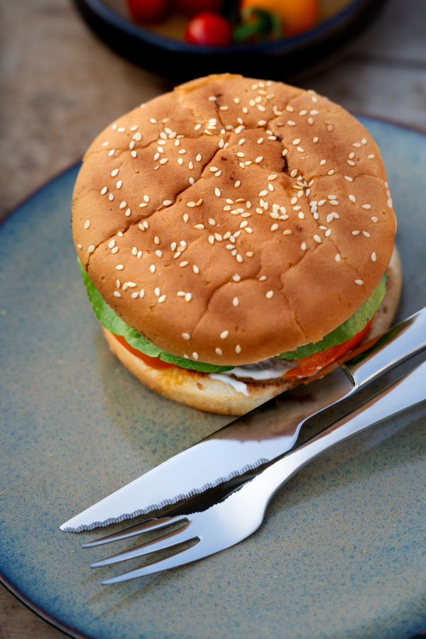 Close up of plate with homemade grilled hamburger and cutlery.