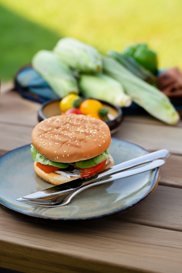 Close up of plate with homemade grilled hamburger and cutlery.