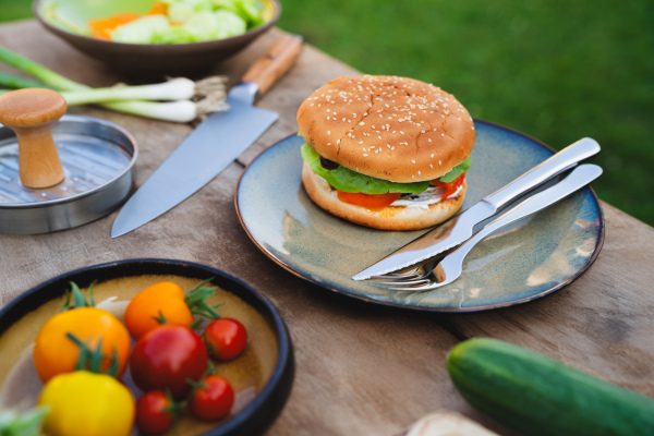 Close up of plate with homemade grilled hamburger and cutlery.