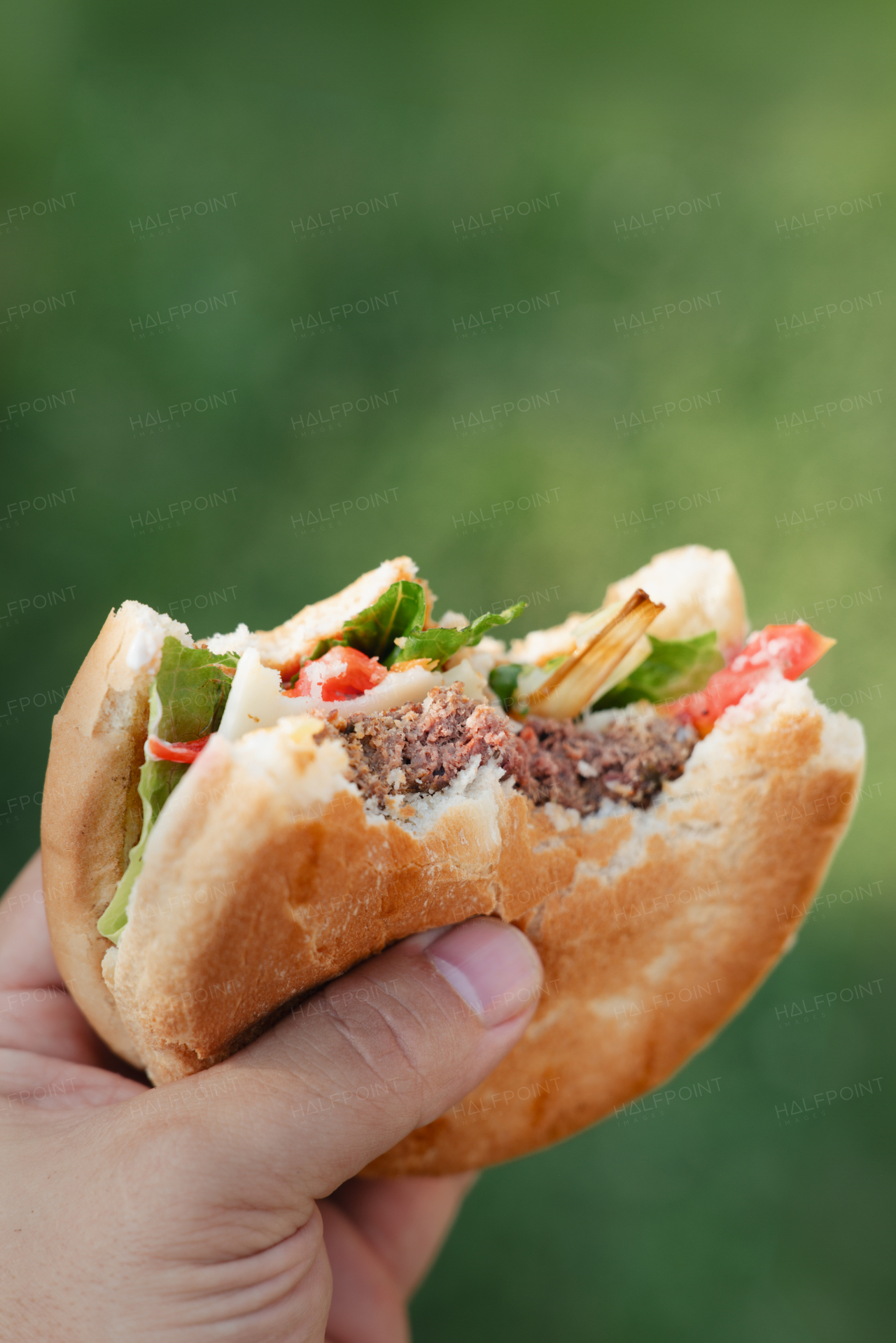 Hand holding homemade grilled hamburger with big bite.