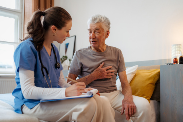 Young nurse taking care of elderly senior in his home.