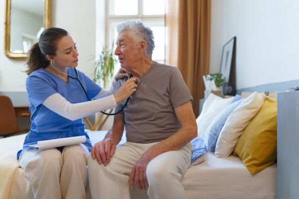 Young nurse taking care of elderly senior in his home.