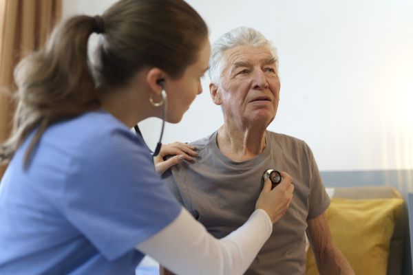 Young nurse taking care of elderly senior in his home.