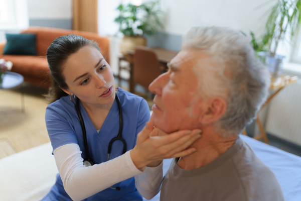 Doctor examine neck lymph nodes. Young nurse taking care of elderly senior in his home.