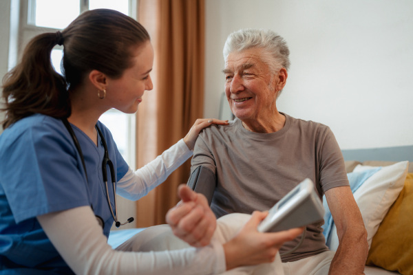 Young nurse taking care of elderly senior in his home.