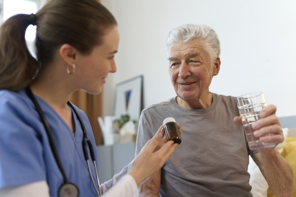 Nurse giving pills senior man in his apartment.