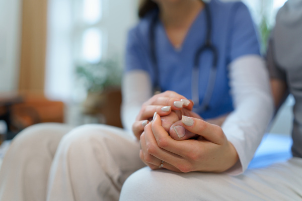 Close up of nurse holding hand of senior client, consoling him.