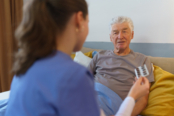 Nurse giving pills senior man in his apartment.