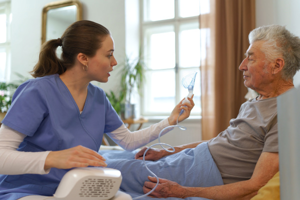 Young nurse taking care of elderly senior in his home.