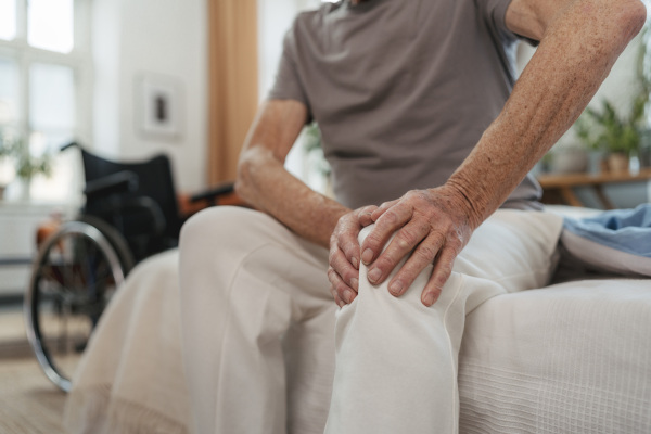 Close-up of senior man with knee pain sitting on bed.