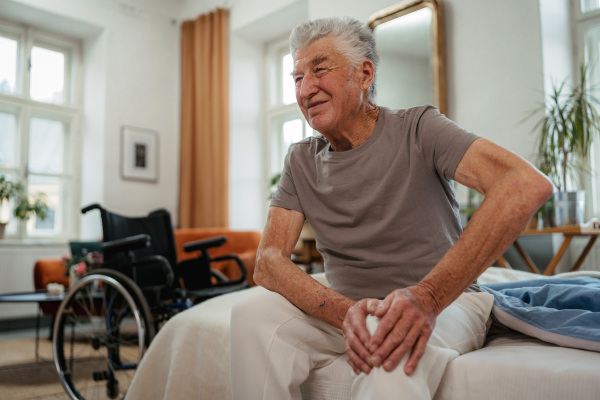 Portrait of senior man with knee pain sitting on bed.