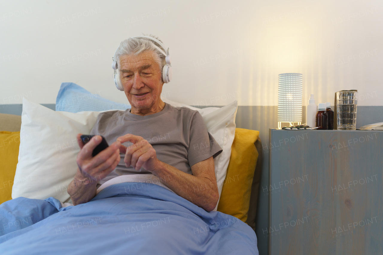 Senior man lying in a bed and enjoying music trough headphones.