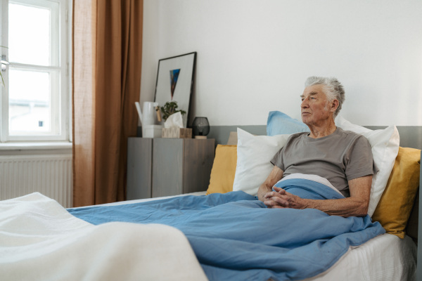 Senior man sitting alone in a bed, concept of loneliness and mental health.