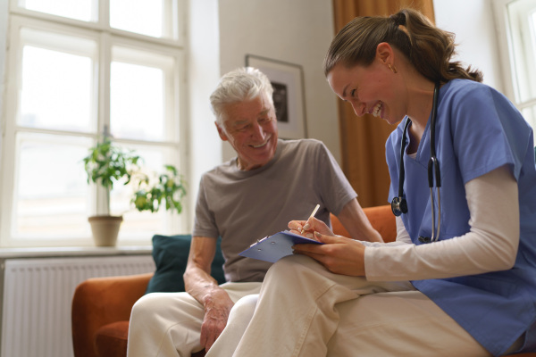 Young nurse taking care of elderly senior in his home.