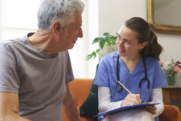 Young nurse taking care of elderly senior in his home.