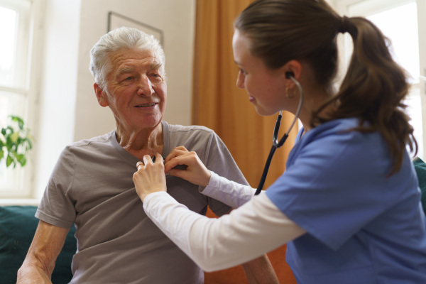 Young nurse taking care of elderly senior in his home.