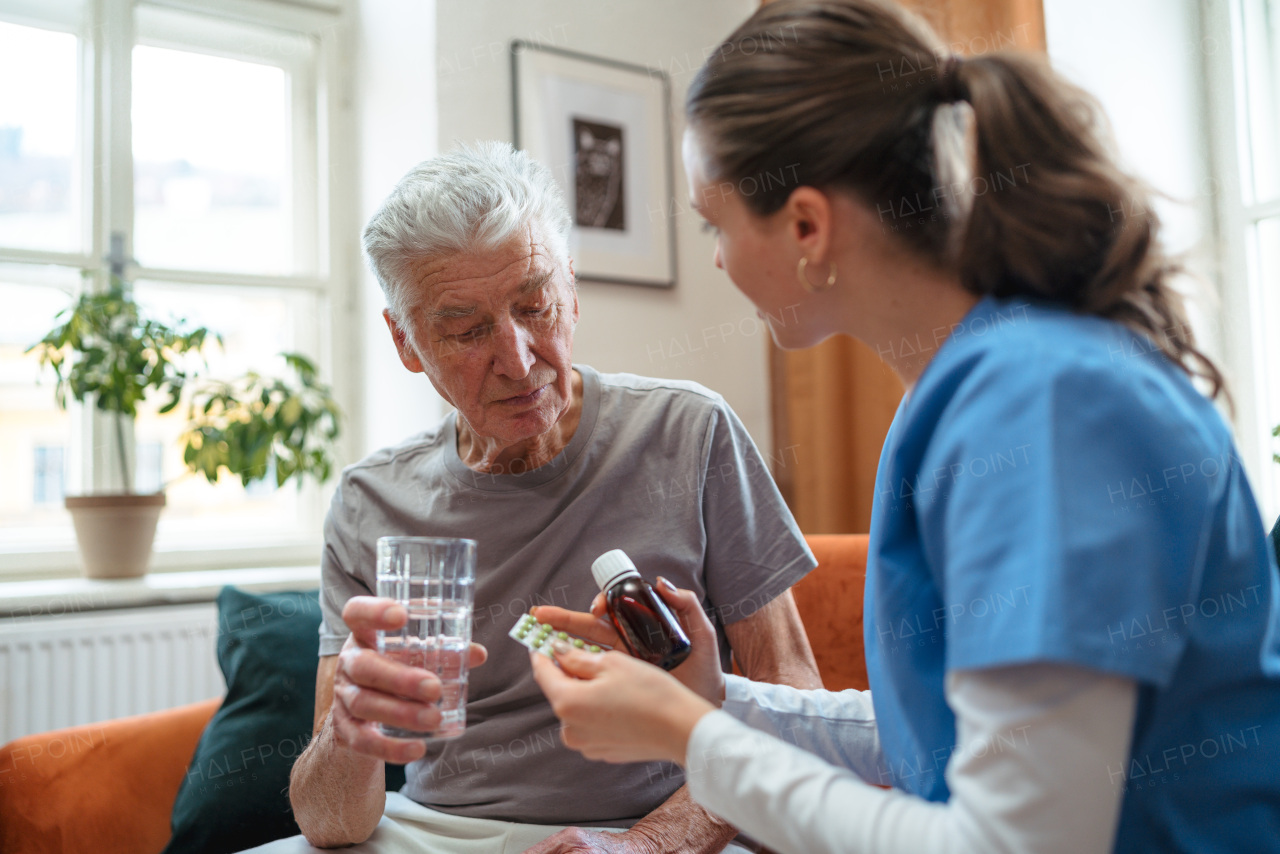 Nurse giving pills senior man in his apartment.