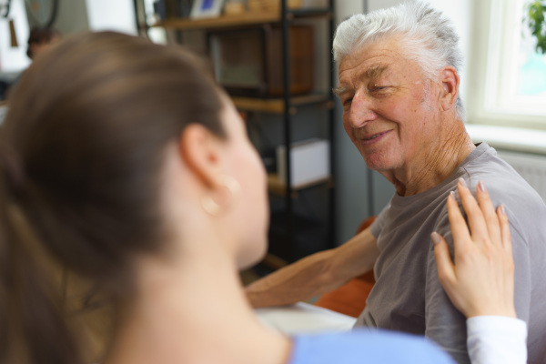 Young nurse taking care of elderly senior in his home.