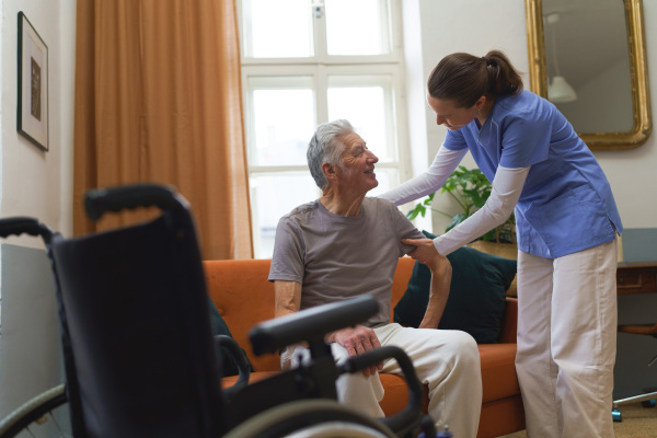 Young nurse taking care of elderly senior, helping him with walking.