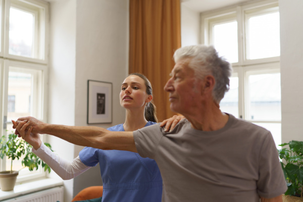 Young nurse doing exercise with senior man in his home.