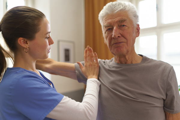 Young nurse doing exercise with senior man in his home.