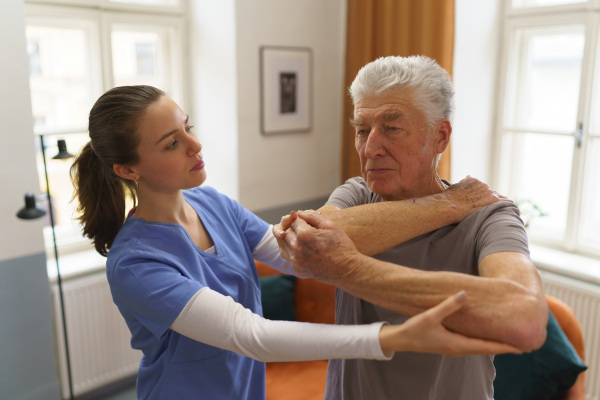 Young nurse doing exercise with senior man in his home.