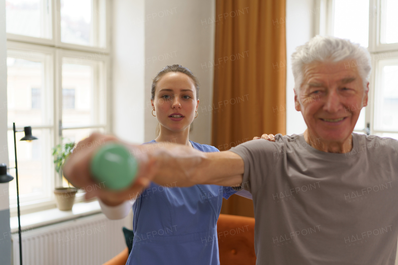 Young nurse doing exercise with senior man in his home.