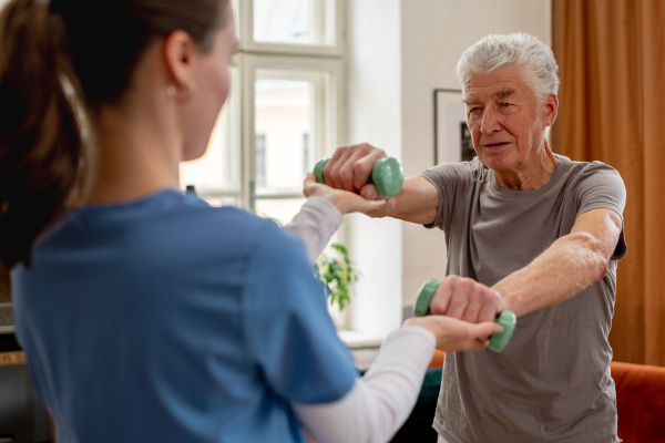 Young nurse doing exercise with senior man in his home.