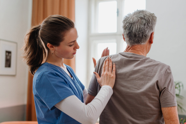 Young nurse doing exercise with senior man in his home.