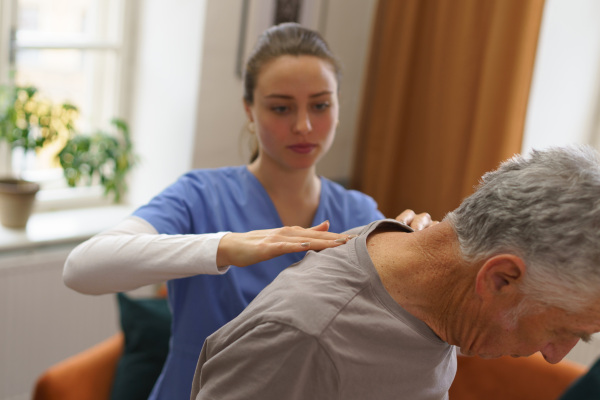 Young nurse doing exercise with senior man in his home.