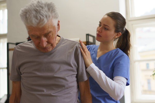 Young nurse doing exercise with senior man in his home.