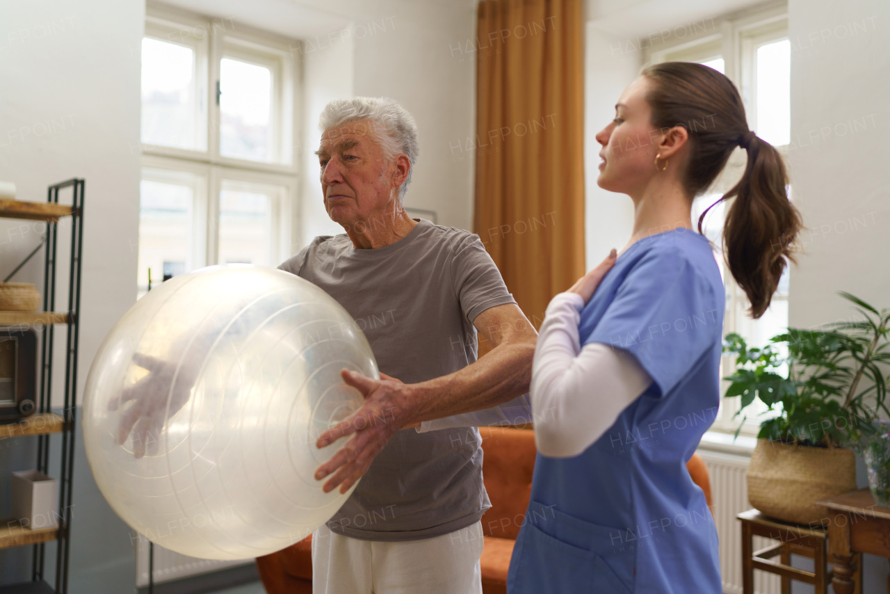 Young nurse doing exercise with senior man in his home.