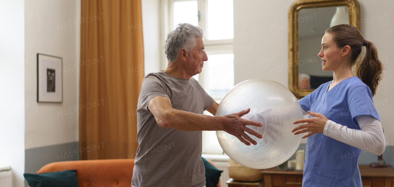 Young nurse doing exercise with senior man in his home.