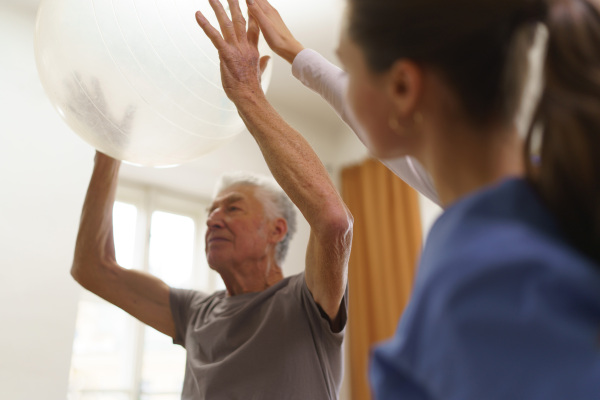 Young nurse doing exercise with senior man in his home.