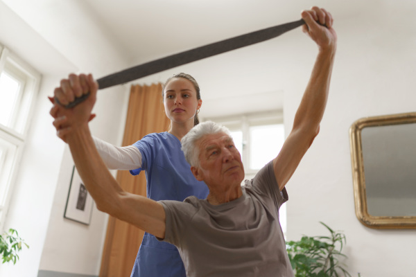 Young nurse doing exercise with senior man in his home.