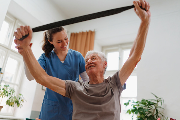 Young nurse doing exercise with senior man in his home.