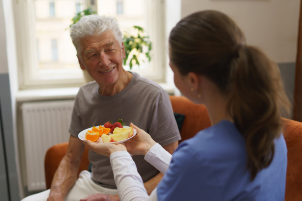 Young caregiver prepared fruit snack for senior man.