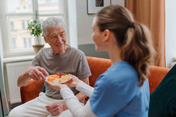 Young caregiver prepared fruit snack for senior man.