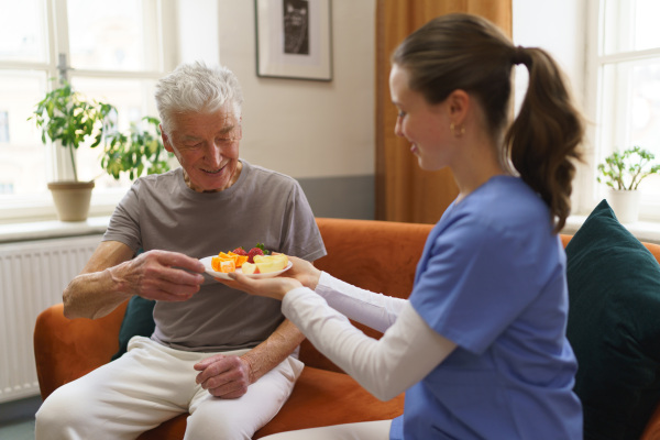 Young caregiver prepared fruit snack for senior man.