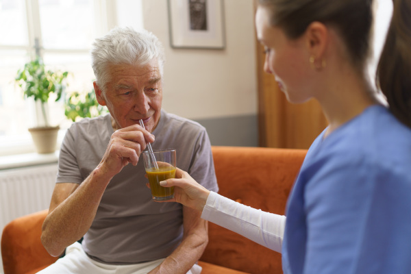 Nurse giving fruit juice to senior man.