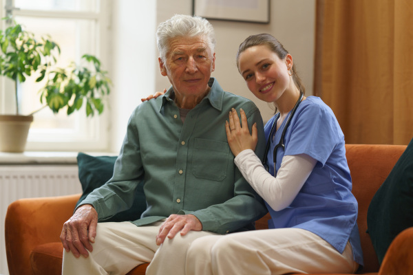 Young nurse taking care of elderly senior in his home.