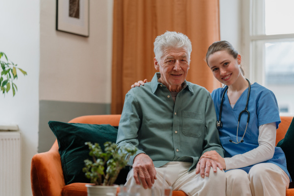 Young nurse taking care of elderly senior in his home.