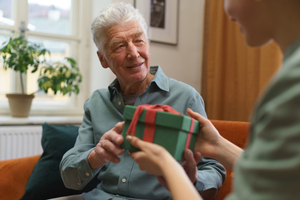 Portrait of senior man giving gift to his caregiver. Smiling elderly man receiving birthday present.