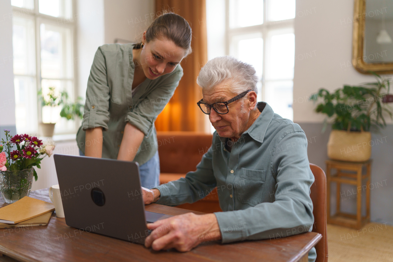 Granddaughter teaching grandfather how to use computer, notebook. Young woman, caregiver showing something to senior on a laptop.