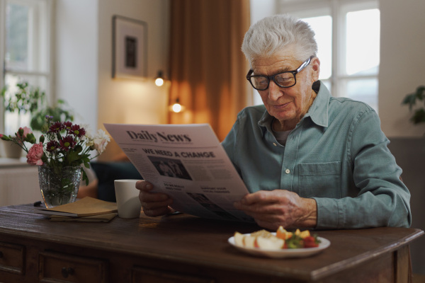 Senior man reading newspaper in the apartment.