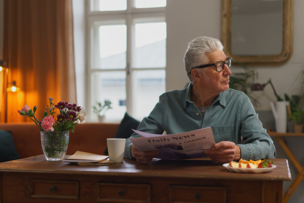 Senior man reading newspaper in the apartment.