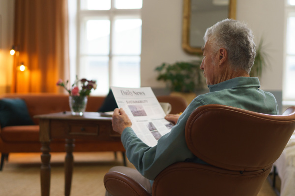 Senior man reading newspaper in the apartment.