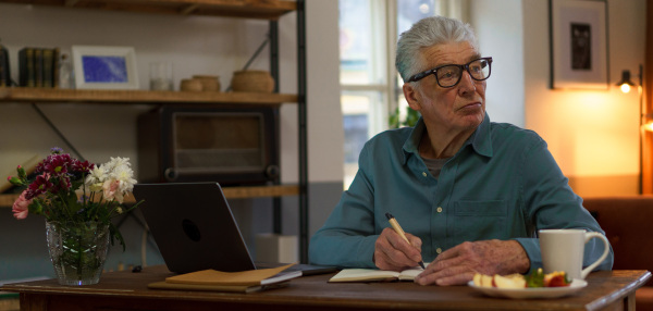 Senior man writing notes in his diary, with opened computer.