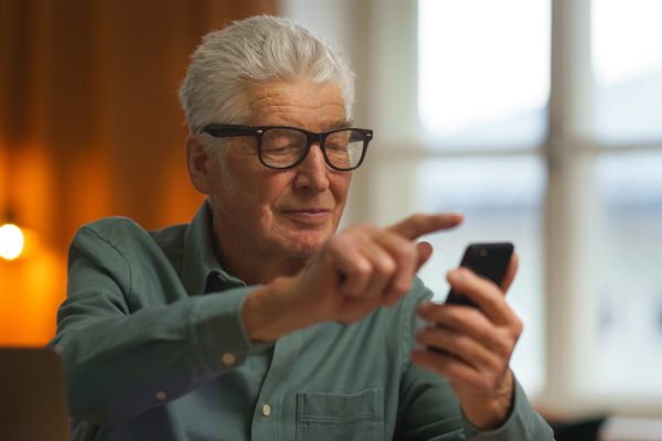 Senior man scrolling his smartphone at his home.